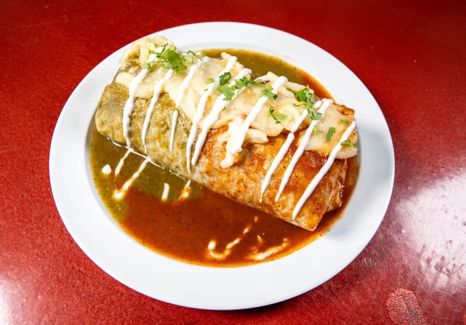 Burrito mojado cubierto de salsa verde y roja con queso derretido